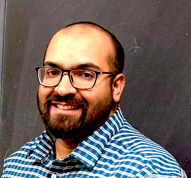 Person wearing a blue-and-white checkered button-down shirt in front of a chalkboard.