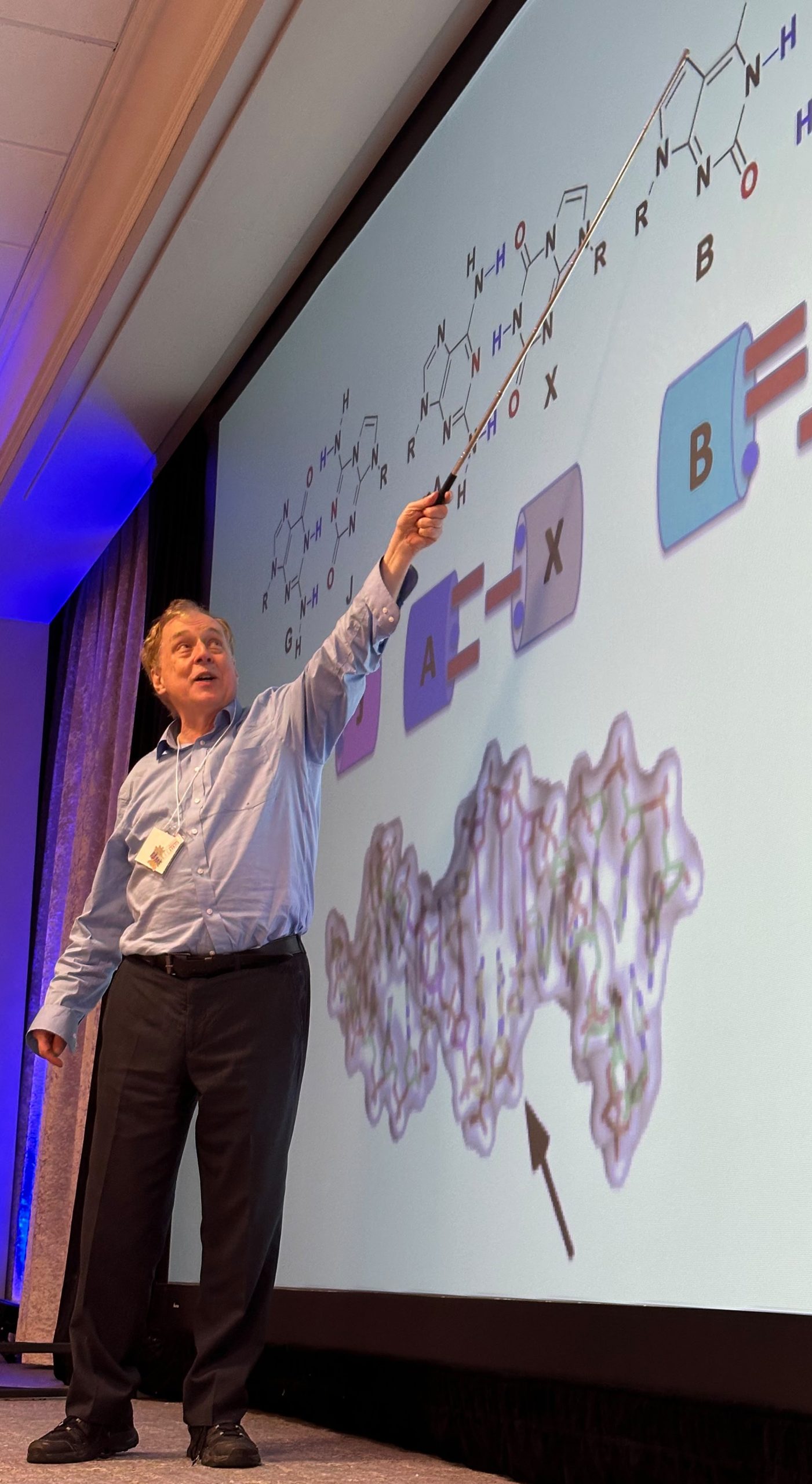 Dr. Benner pointing at the presentation screen during his lecture at FAME 2026